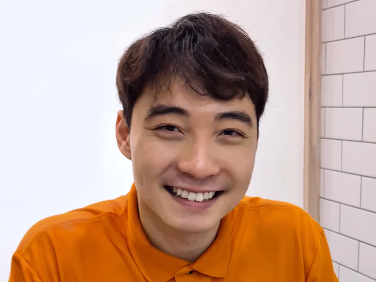 Nigel Ng as Uncle Roger smiling in an orange polo shirt