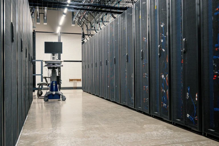 Rows of dark server cabinets beside an aisle with a mobile monitor station in a data center