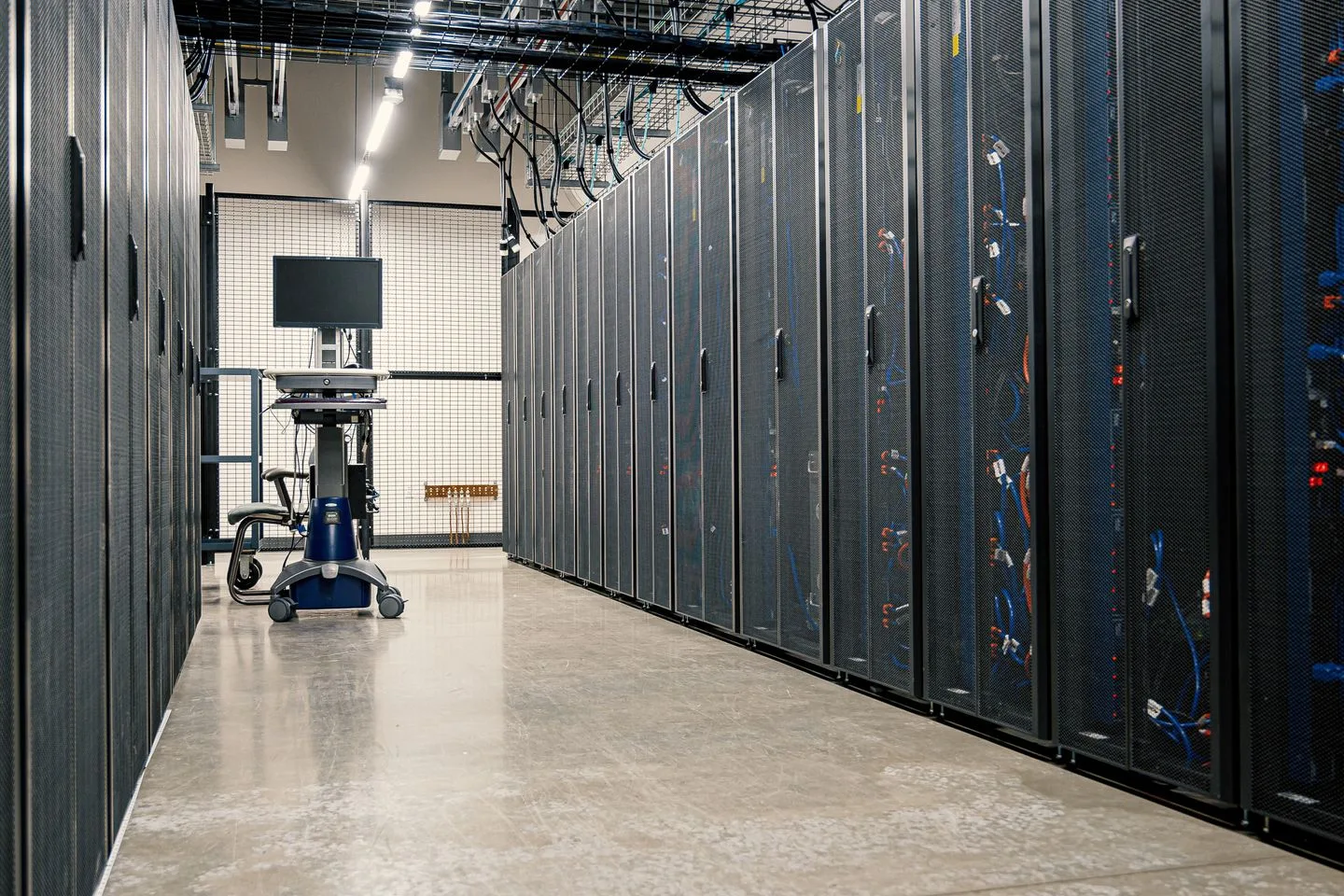 Rows of dark server cabinets beside an aisle with a mobile monitor station in a data center