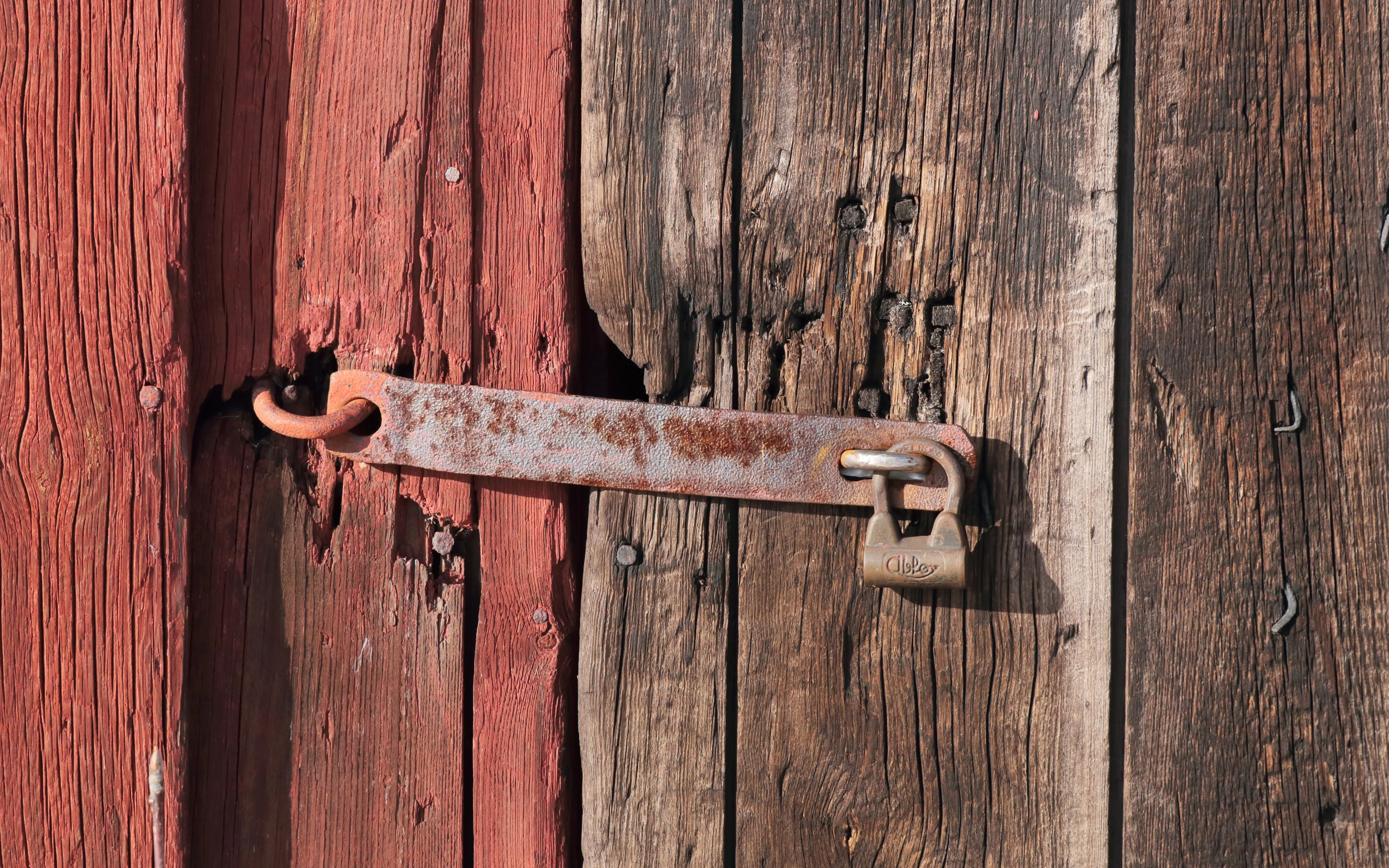 A brass padlock secures a rusty metal hasp across red and unpainted weathered wooden doors