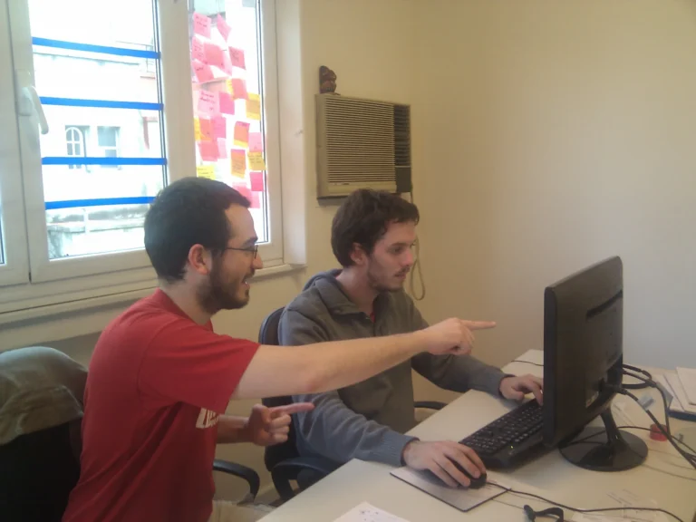 Two programmers looking at a desktop monitor while one points toward the screen