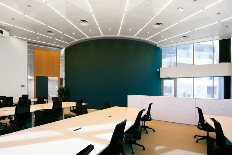 Empty office with white desks, black chairs, a tall green wall and large windows
