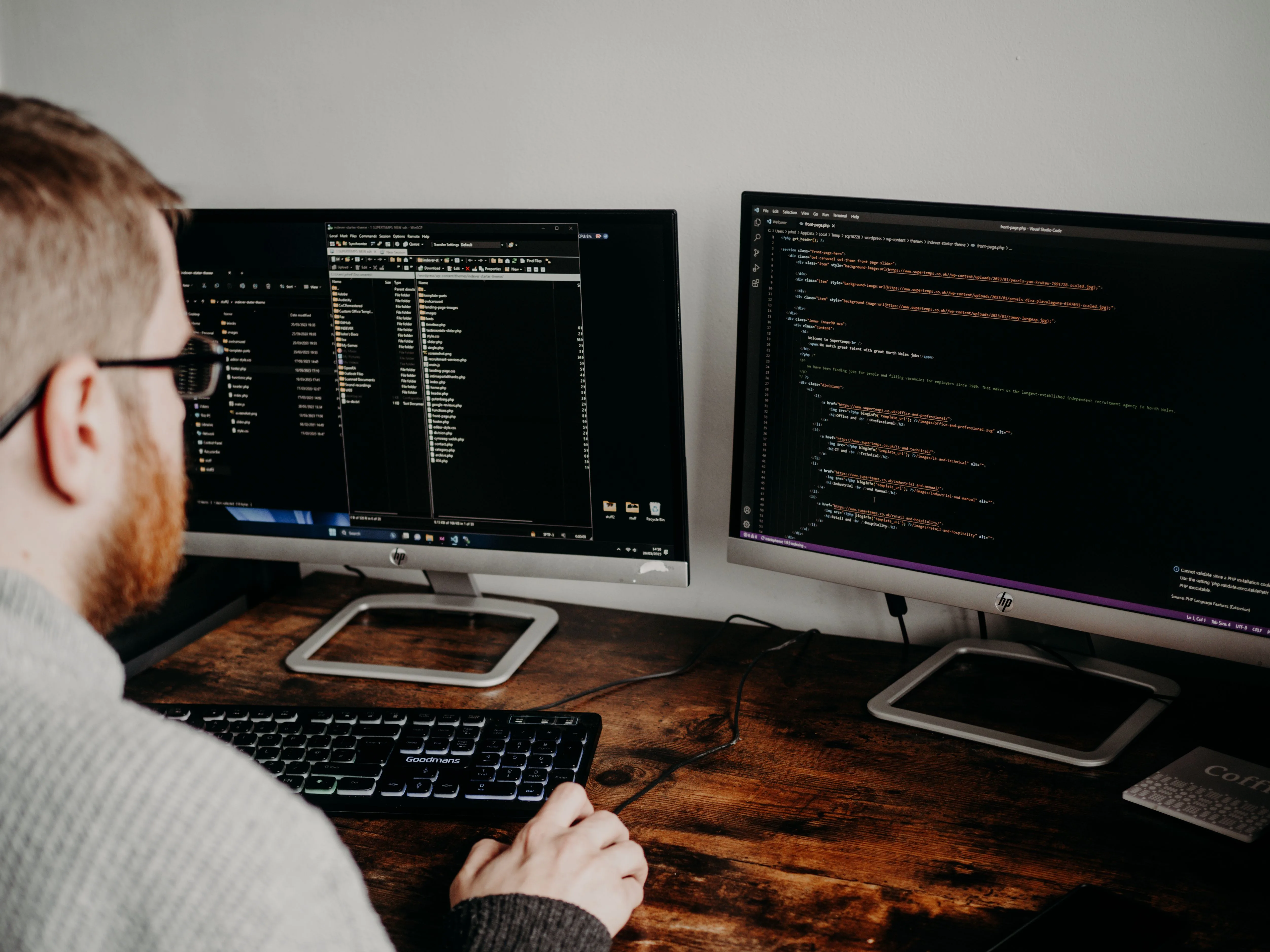 A developer works at two monitors displaying code on a wooden desk