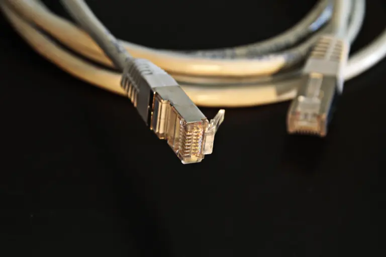 Two gray Ethernet cable plugs rest on a black surface with the nearer connector in sharp focus