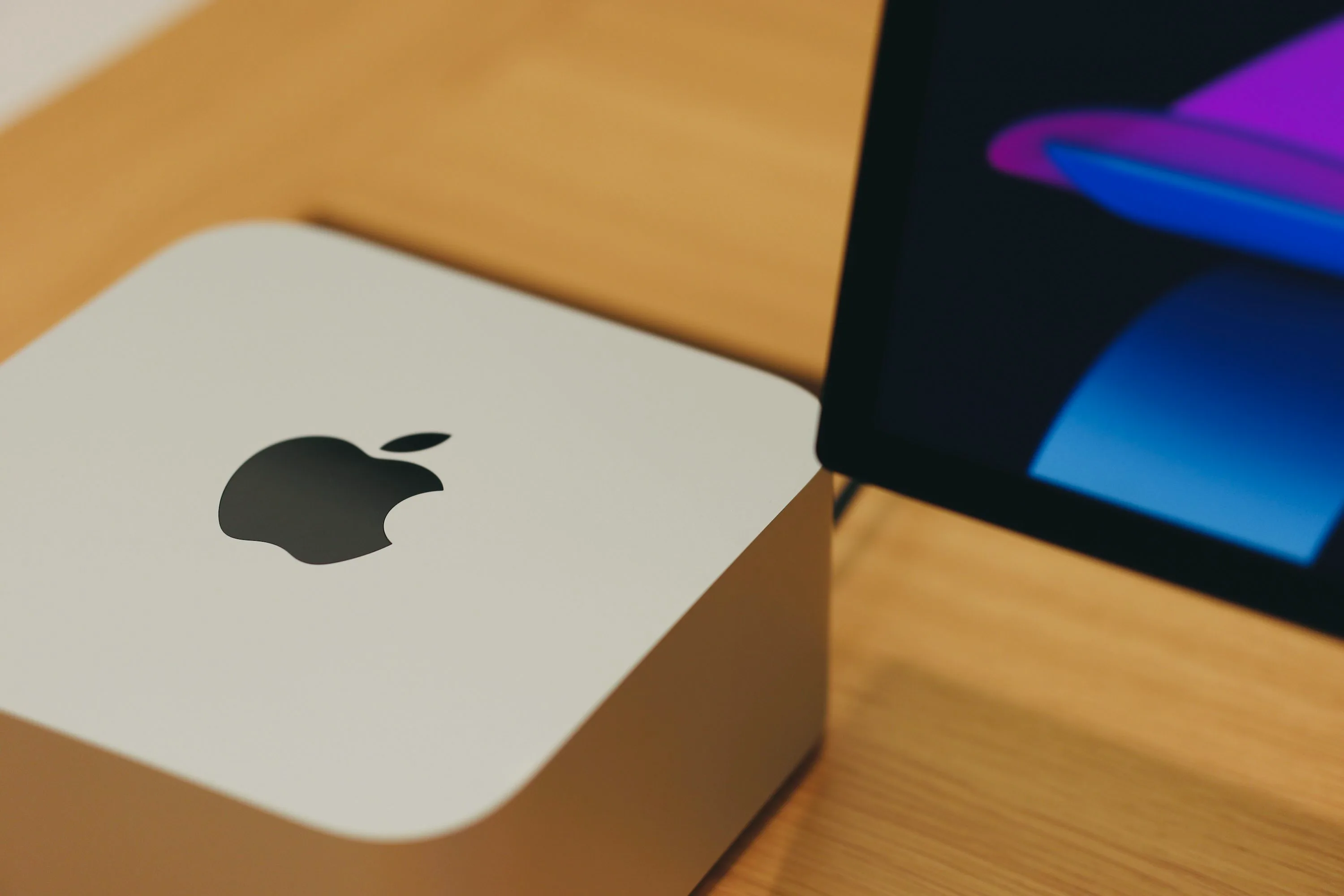 Silver Mac Studio with a black Apple logo beside a display on a wooden table