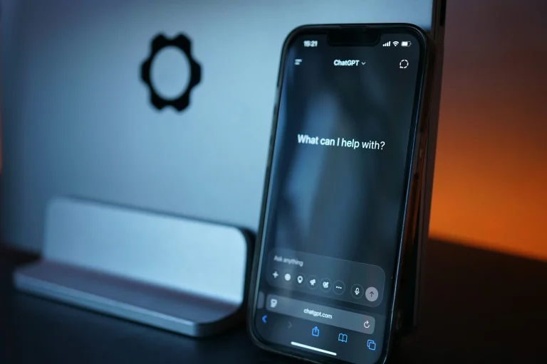 A black smartphone showing the ChatGPT website rests against a laptop in blue and orange light