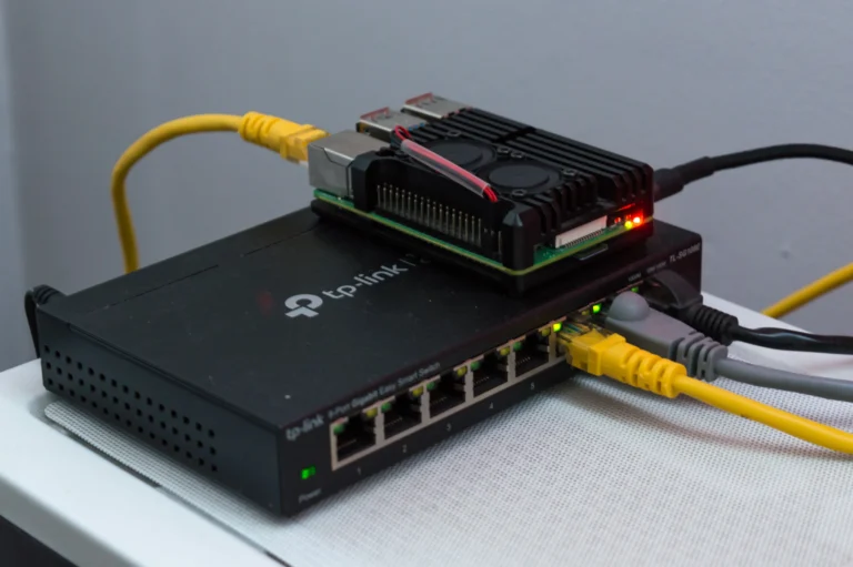 A Raspberry Pi computer with cooling fans sits on a network switch with connected Ethernet cables