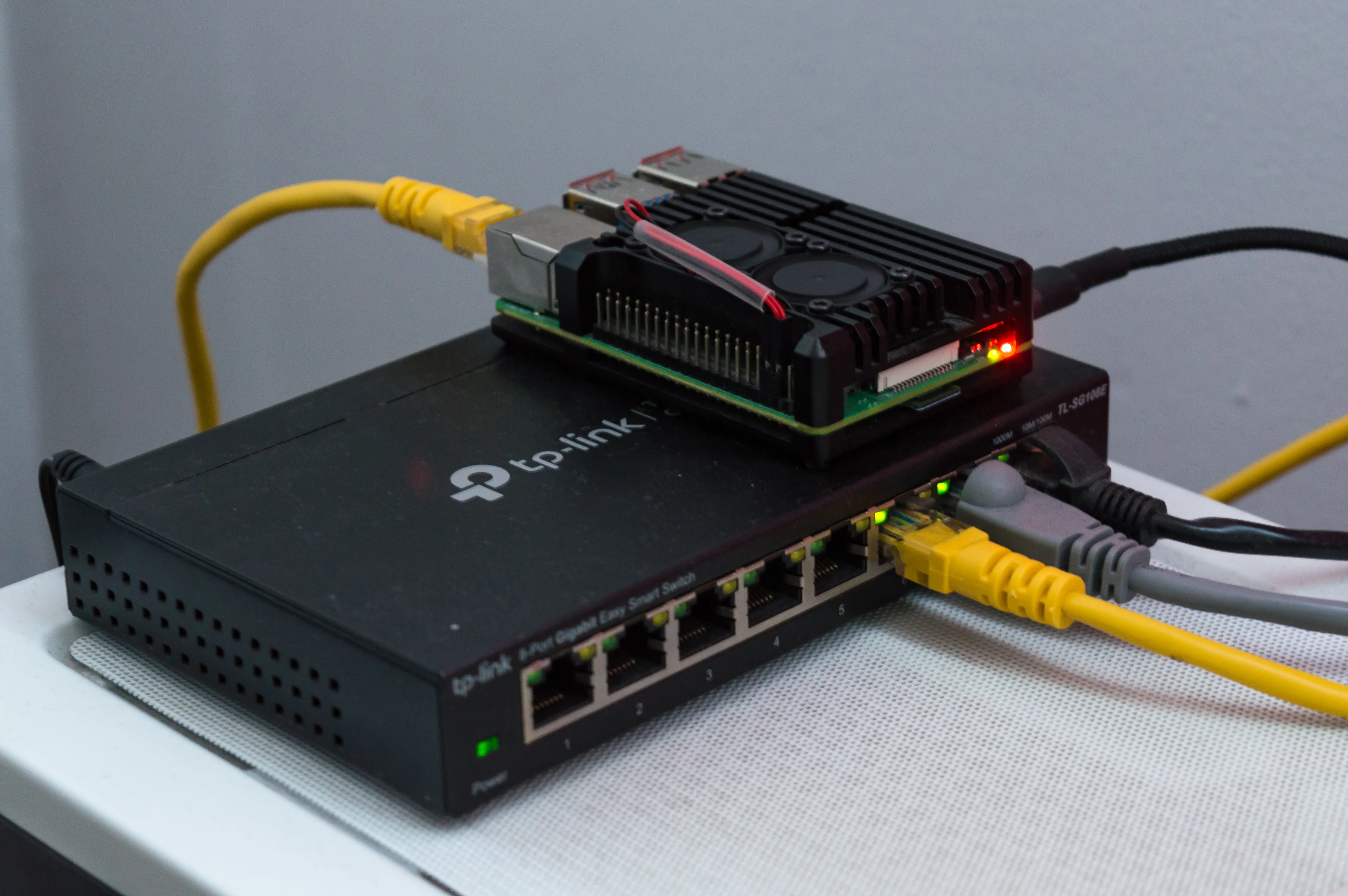 A Raspberry Pi computer with cooling fans sits on a network switch with connected Ethernet cables