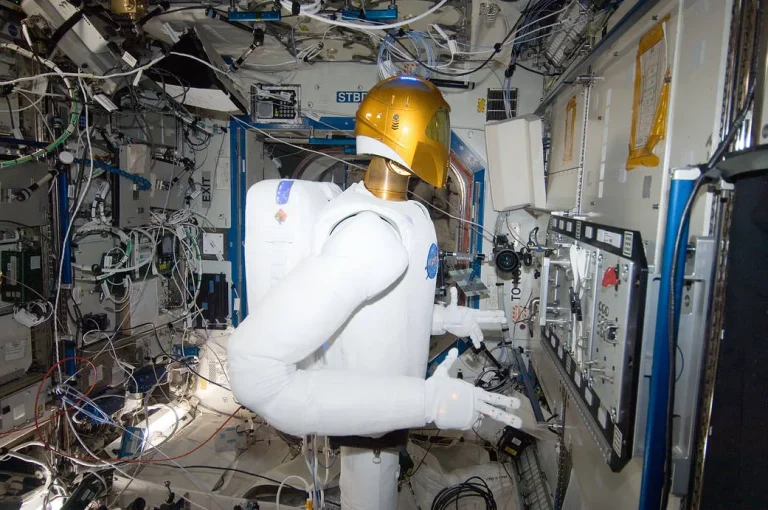 Robonaut 2 with a gold visor and white torso operating a valve task board inside the International Space Station