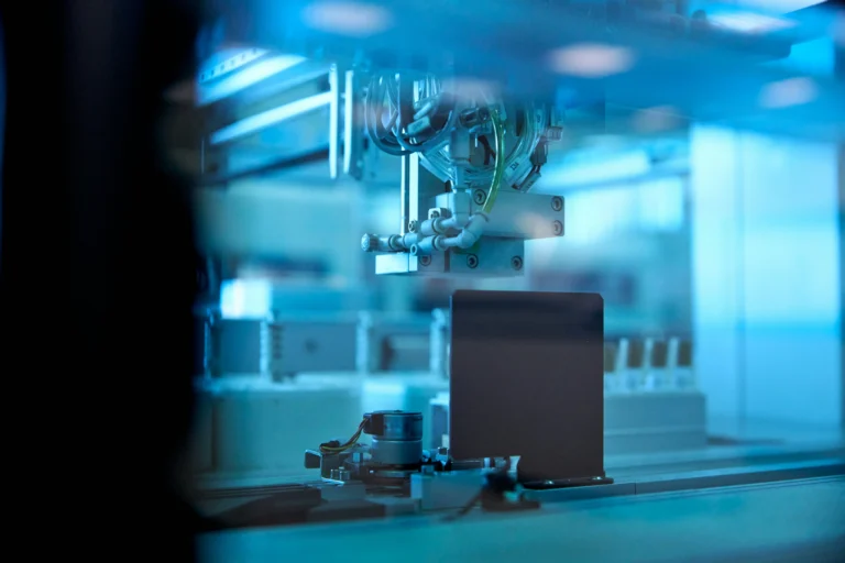 Automated laboratory equipment and a mechanical gripper behind glass under blue lighting