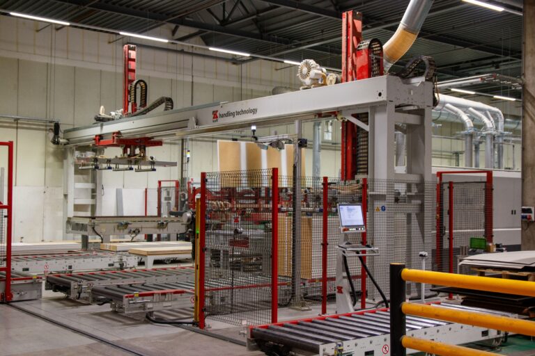 Factory conveyor rollers and handling machinery behind red and black safety fencing