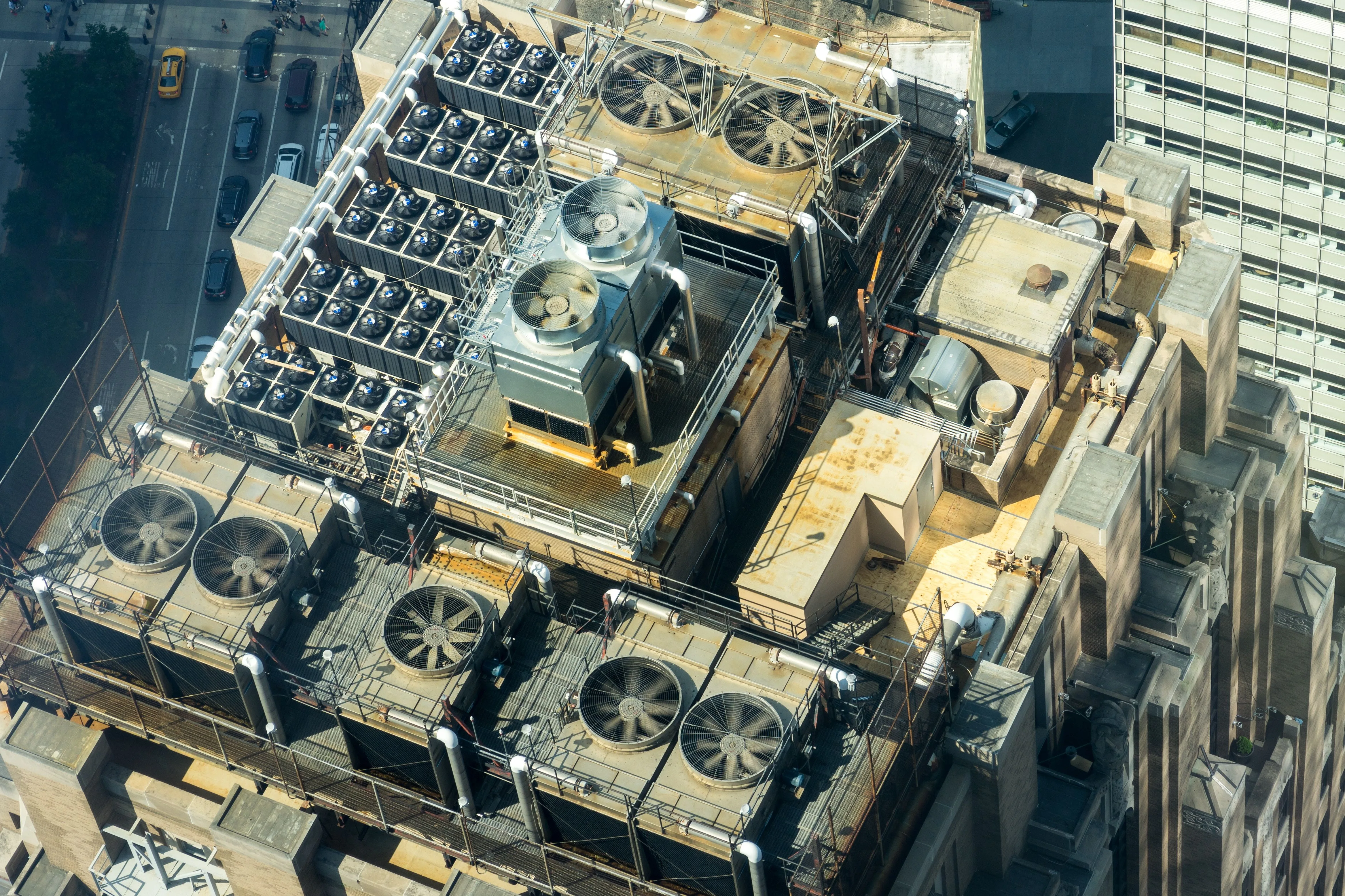 Rows of large cooling fans and pipes on an urban building rooftop