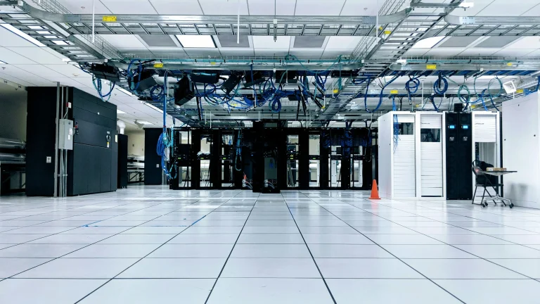 Server room with black and white equipment cabinets beneath overhead blue cables