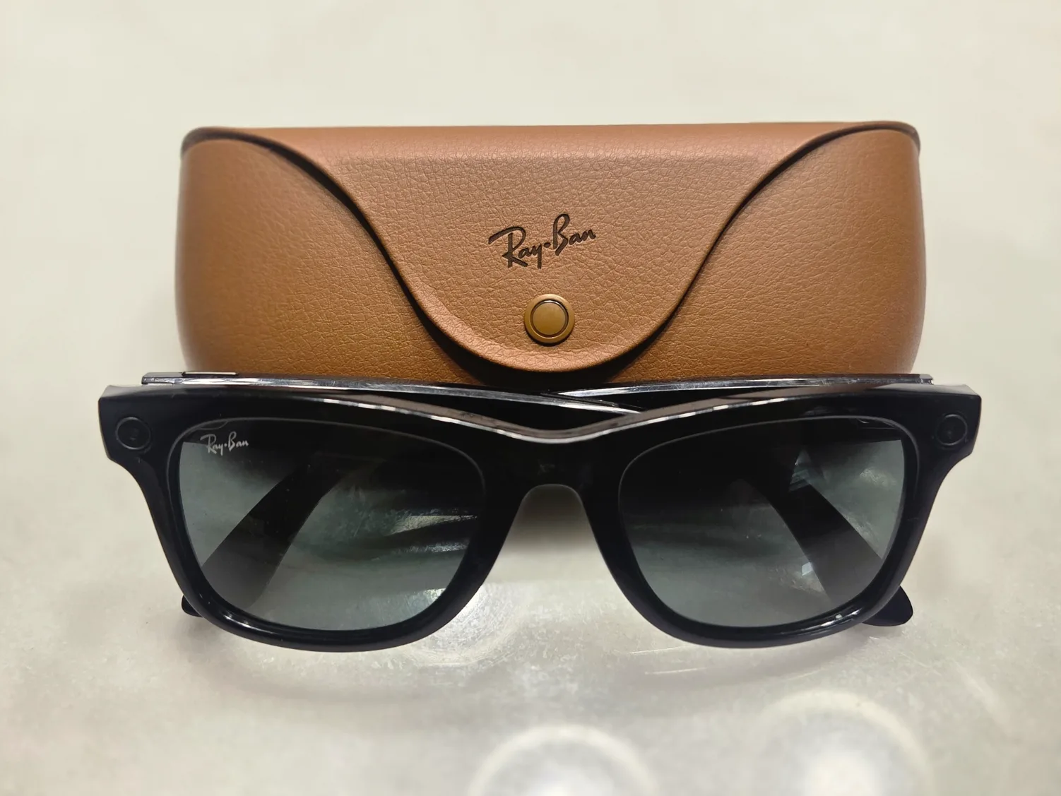 Black smart glasses in front of a brown charging case