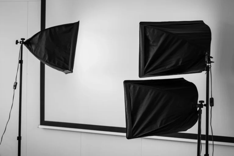 Three black photography softboxes on stands face a blank screen