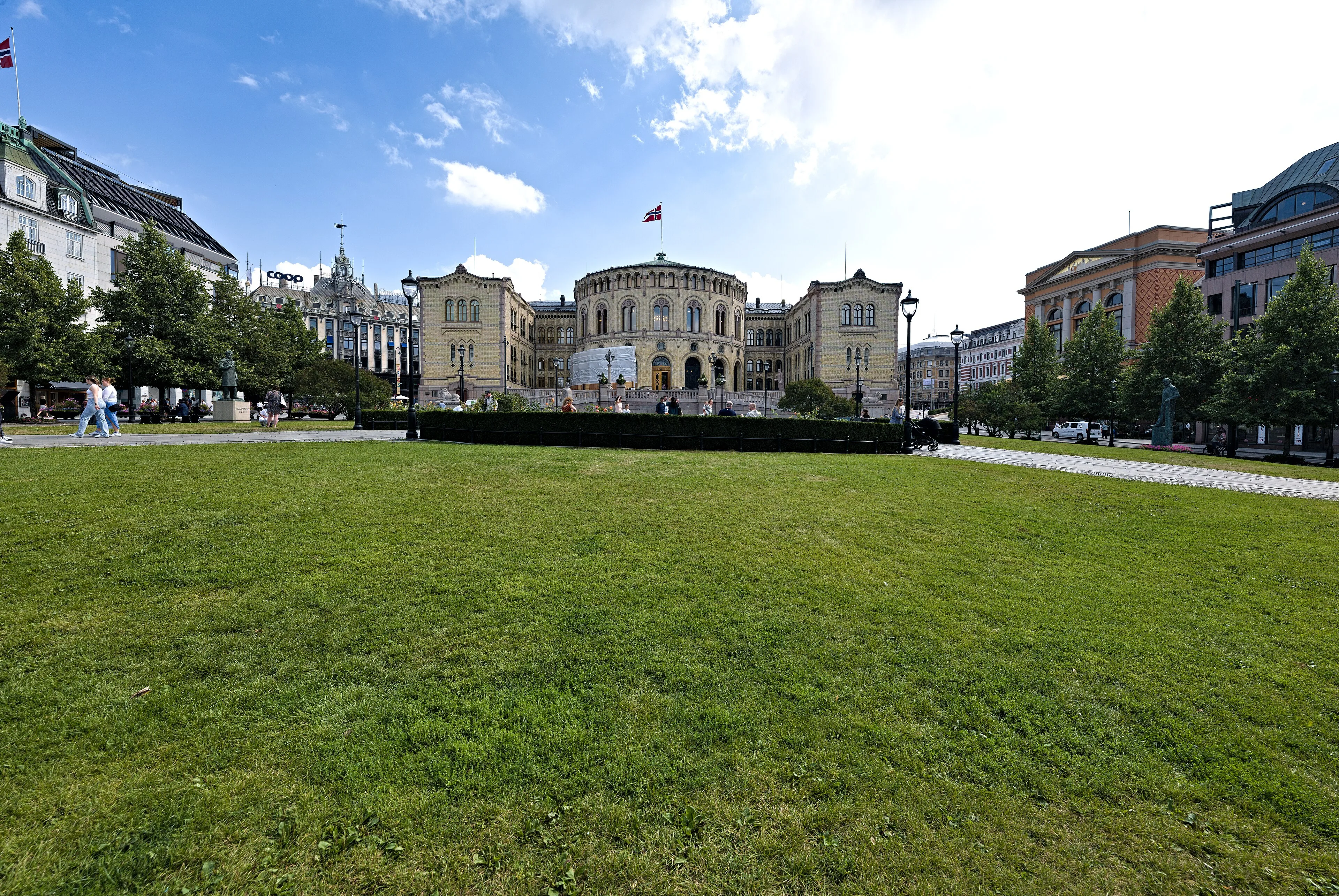 Norway’s parliament building in Oslo stands beyond a green lawn beneath a blue sky