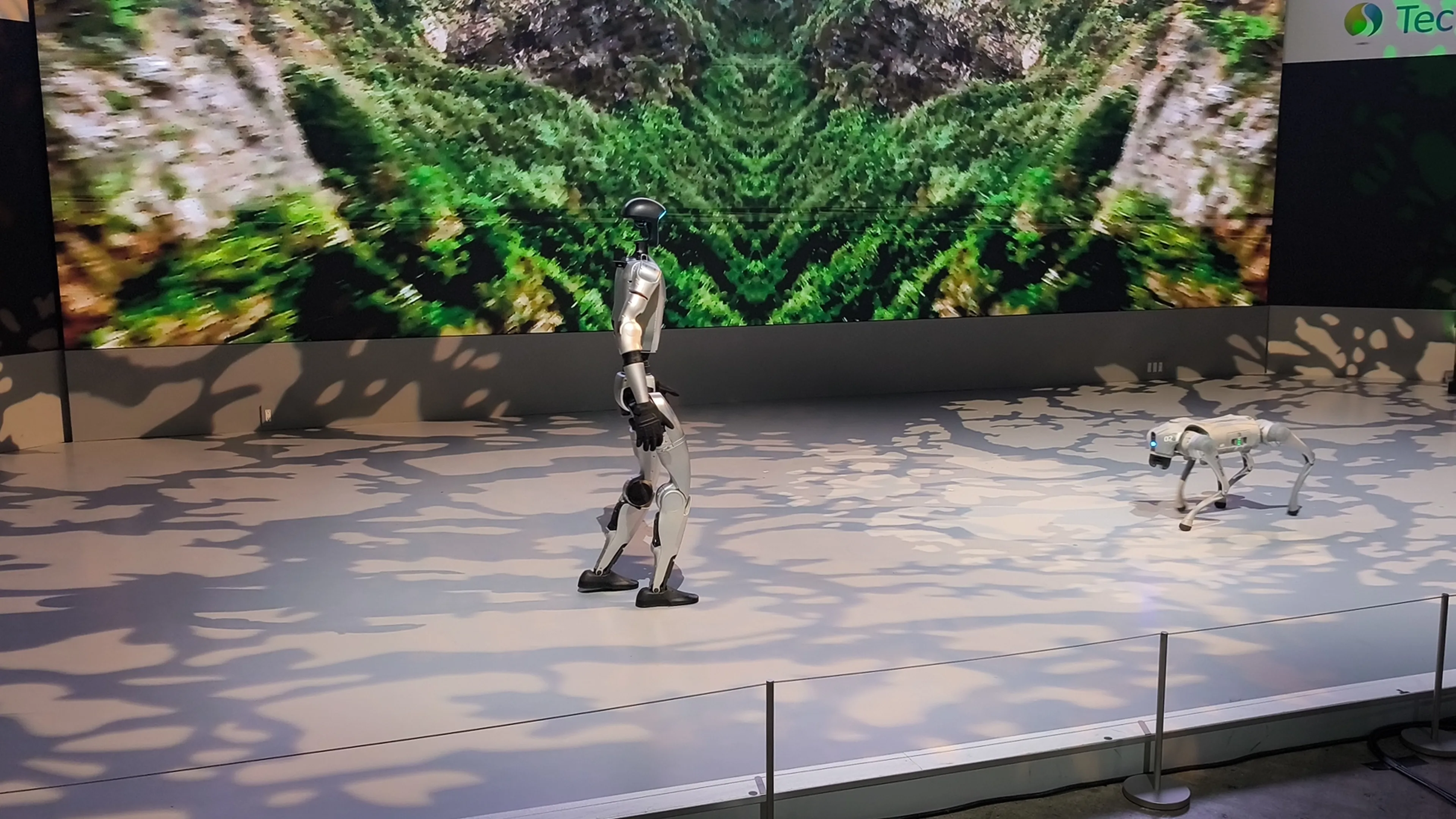 A Unitree G1 humanoid robot and a Go2 robot on an exhibition stage.