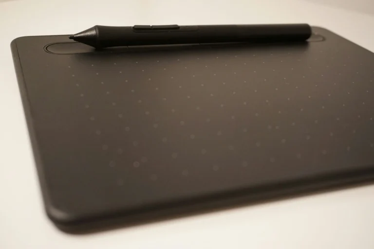 A black stylus rests across the upper edge of a dark drawing tablet on a pale surface