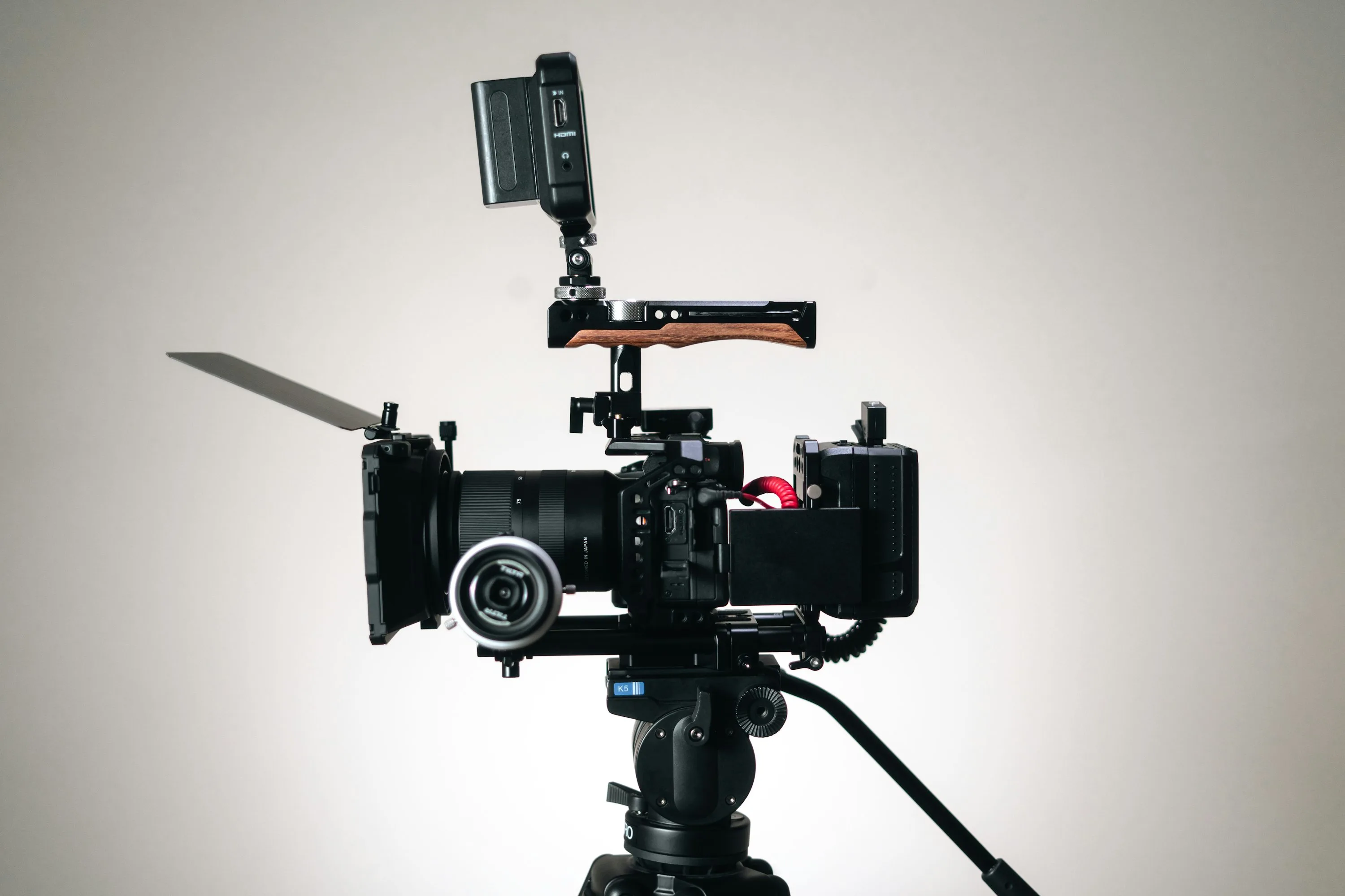 A professional video camera rig mounted on a tripod against a pale wall