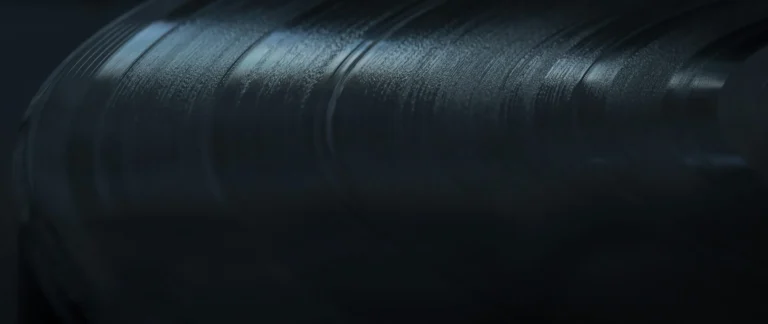 Light reflects across curved grooves on a dark vinyl record