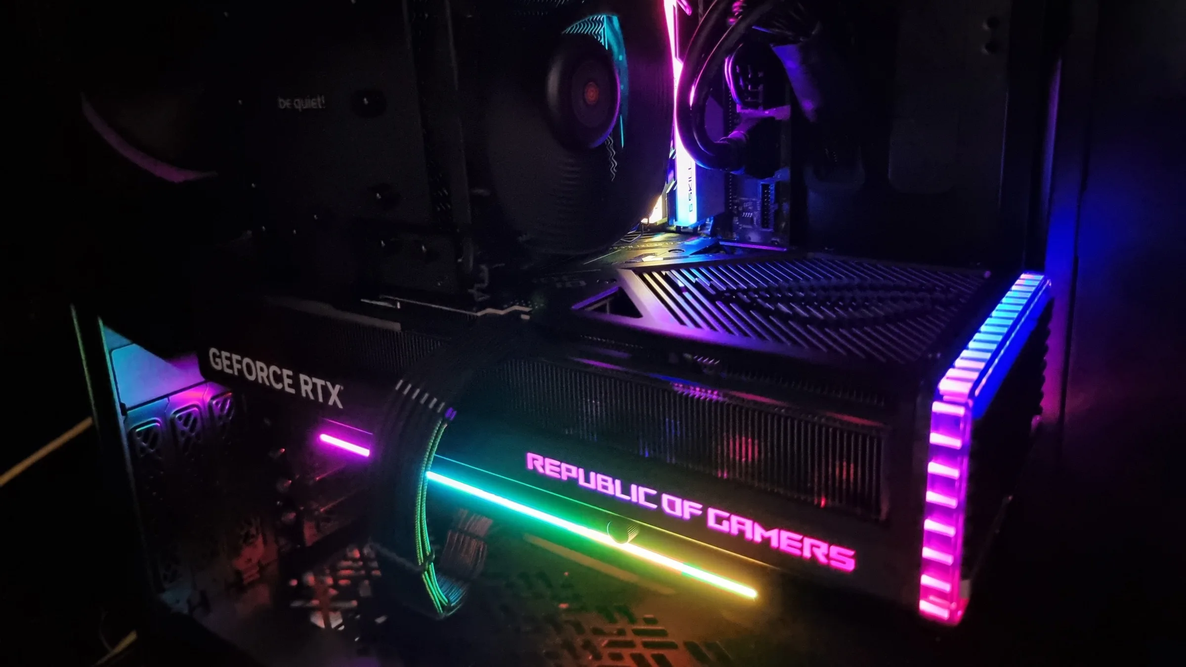 An illuminated GeForce RTX graphics card inside a desktop computer with a large cooling fan and colorful memory lighting