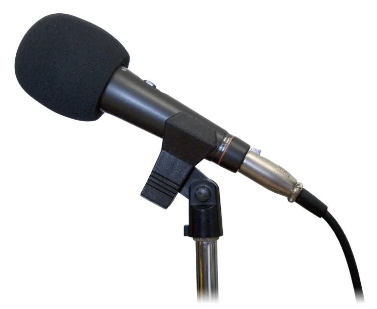 A black studio microphone with a foam windscreen on a stand against a white background