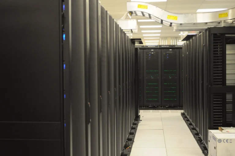 Black server racks flank an aisle beneath overhead cable trays at NERSC