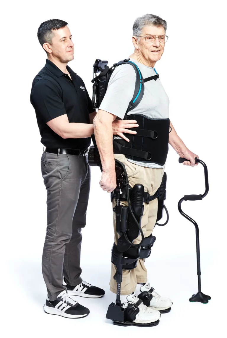 Person wearing an EksoNR exoskeleton beside a therapist against a white background