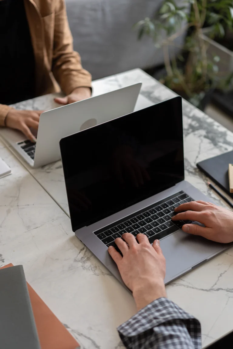 Two people using laptops across a pale marble table